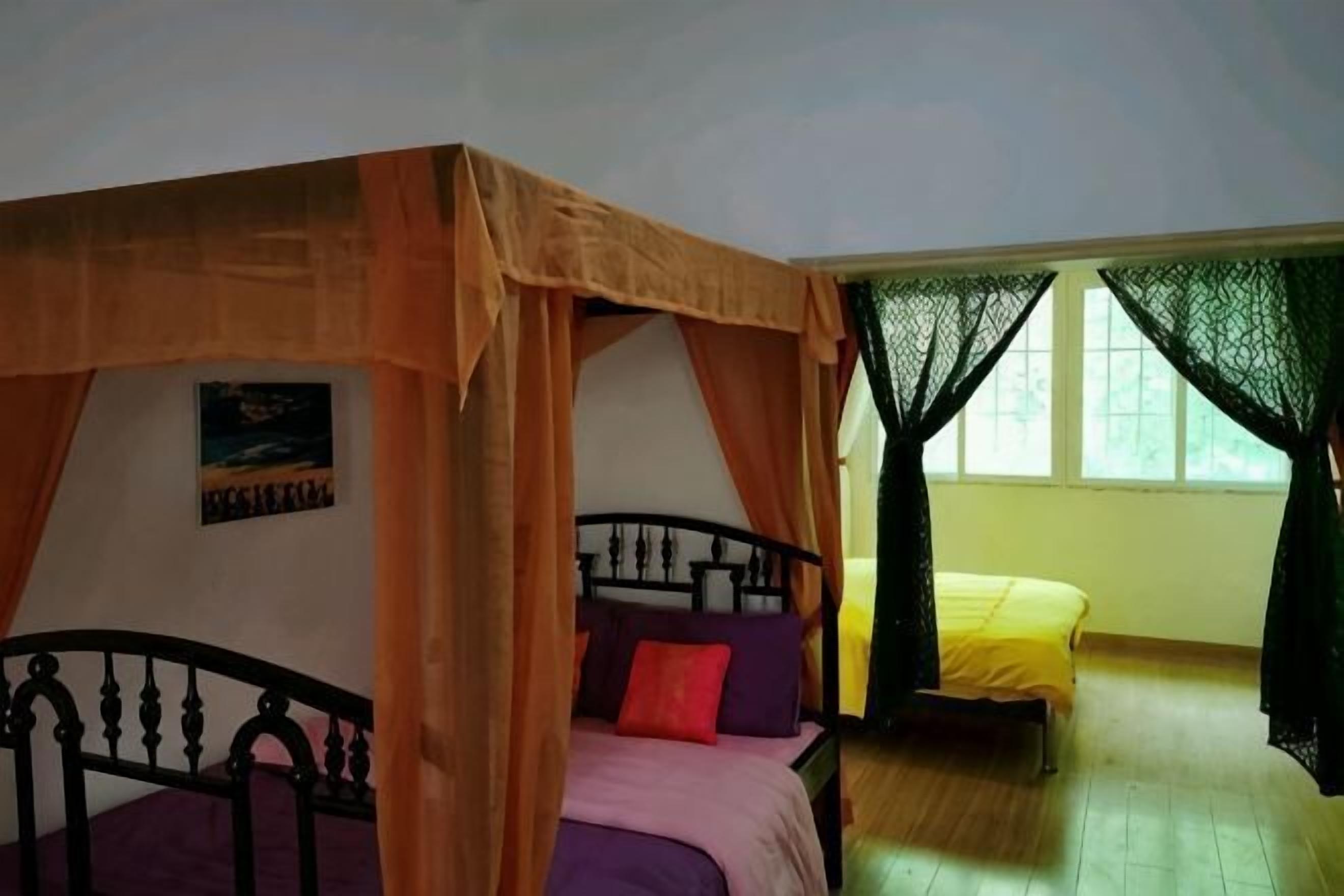A room with a bed under a canopy, a bench, and a window with curtains.