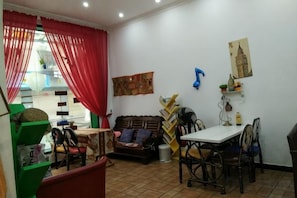 A dining area with a table and chairs, a sofa, and a window with red curtains. - manmancoffee (Zixing)