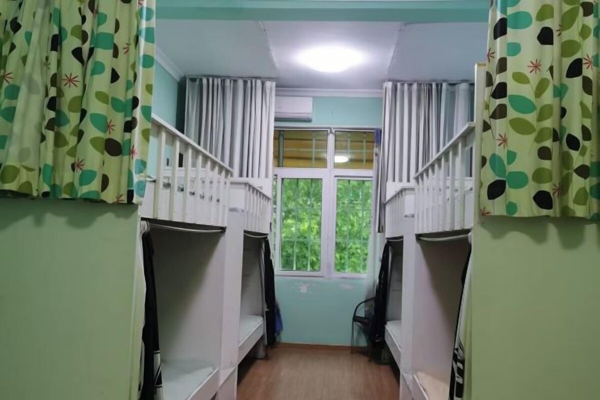 A dormitory room with bunk beds, a window with curtains, and an air conditioning unit.