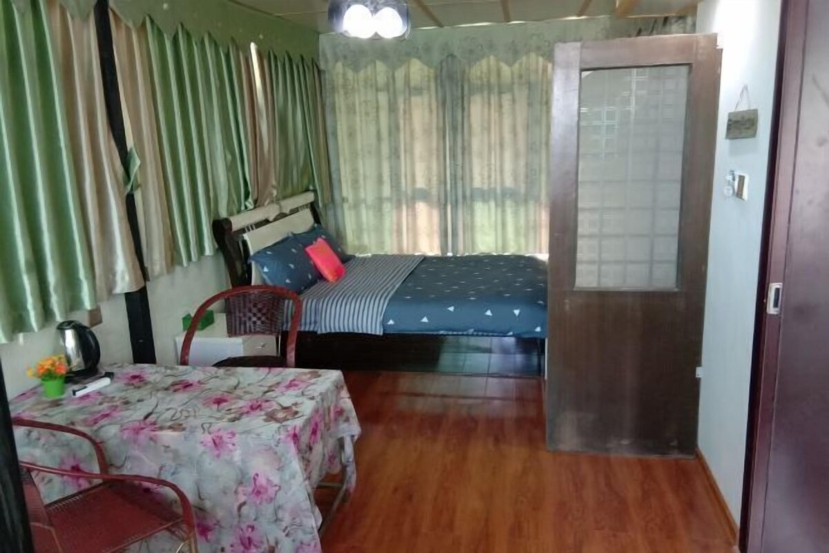 Una habitación con una cama, una mesa con mantel floreado, una silla y una puerta.