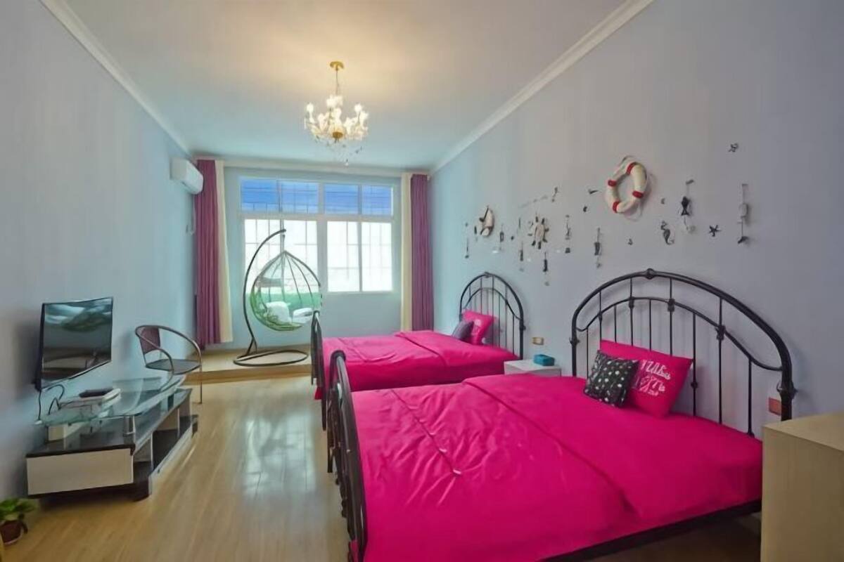 Ein Schlafzimmer mit zwei Betten, einem Fernseher, einer Glasschrank, einem Hängesessel und einem großen Fenster.