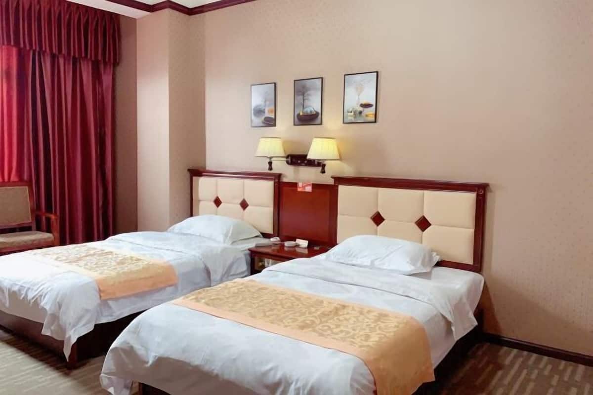 A hotel room with two beds, a nightstand, a lamp, and a chair. There are three framed pictures on the wall.