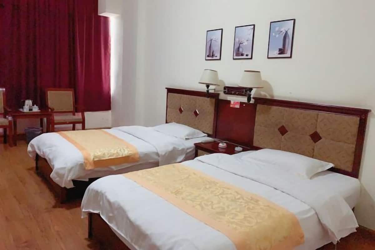 A hotel room with two beds, a desk, a chair, and a window with red curtains.