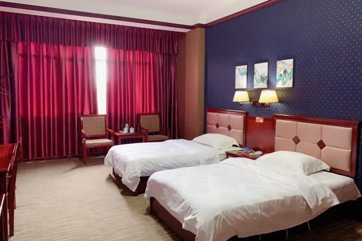 A hotel room with two beds, a desk, a chair, and a window with red curtains.