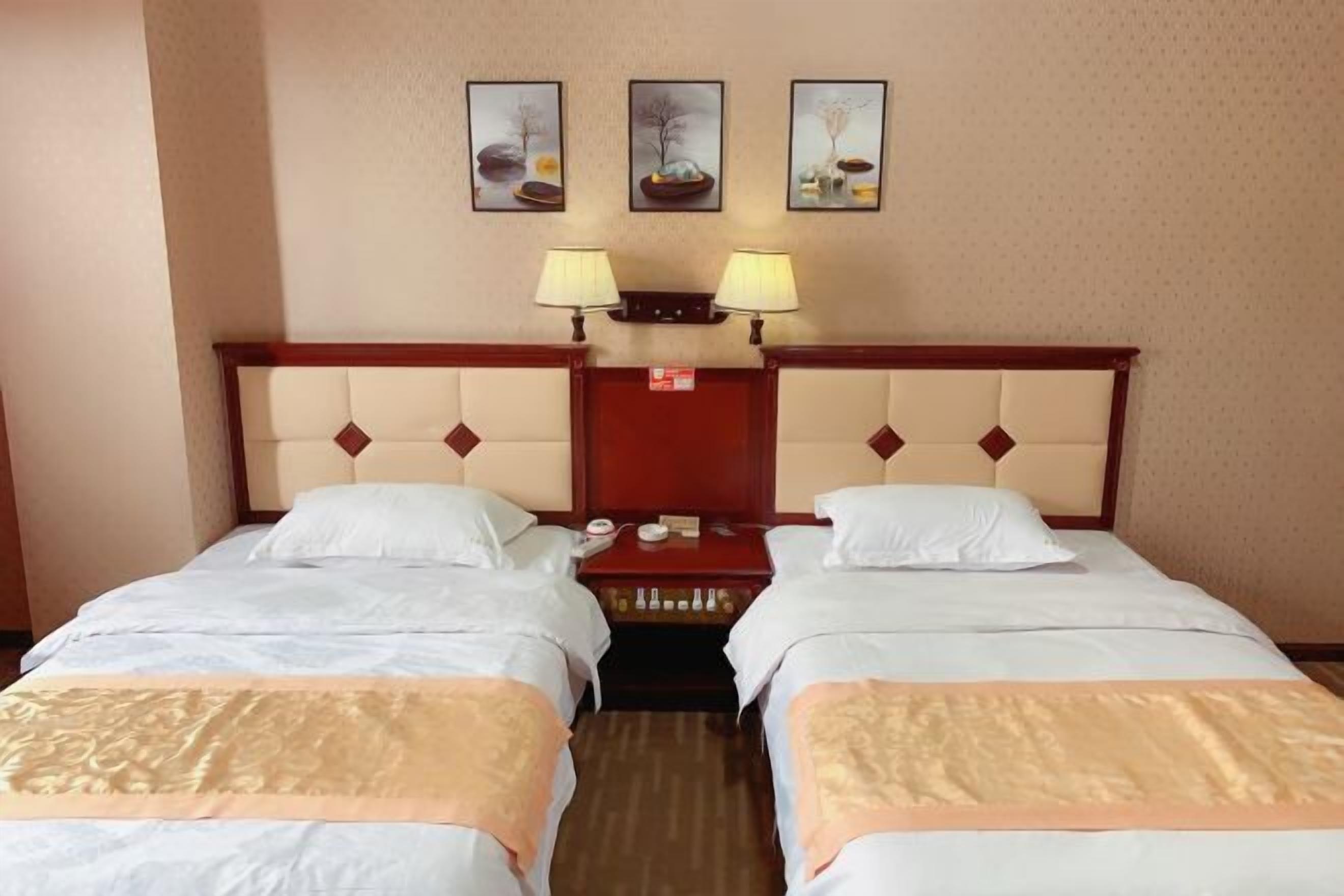 A hotel room with two beds, a wooden headboard, a nightstand, and three wall-mounted lamps.