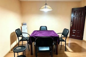 A dining area with a table, four chairs, a purple tablecloth, a hanging light fixture, and a door in the background. - Jinxinbinguan (Shizong)