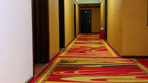 A hotel hallway with a patterned carpet, a door at the end, and a trash bin to the right. - Jinxinbinguan (Shizong)