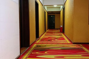 Un pasillo con alfombra estampada, puertas a ambos lados y un extintor a la derecha.