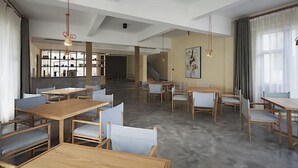 Un comedor amplio con mesas y sillas de madera, una escalera al fondo y luces colgantes.
