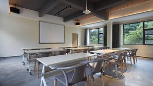 Una sala de conferencias moderna con mesas, sillas, ventanas amplias y una pantalla de proyector.