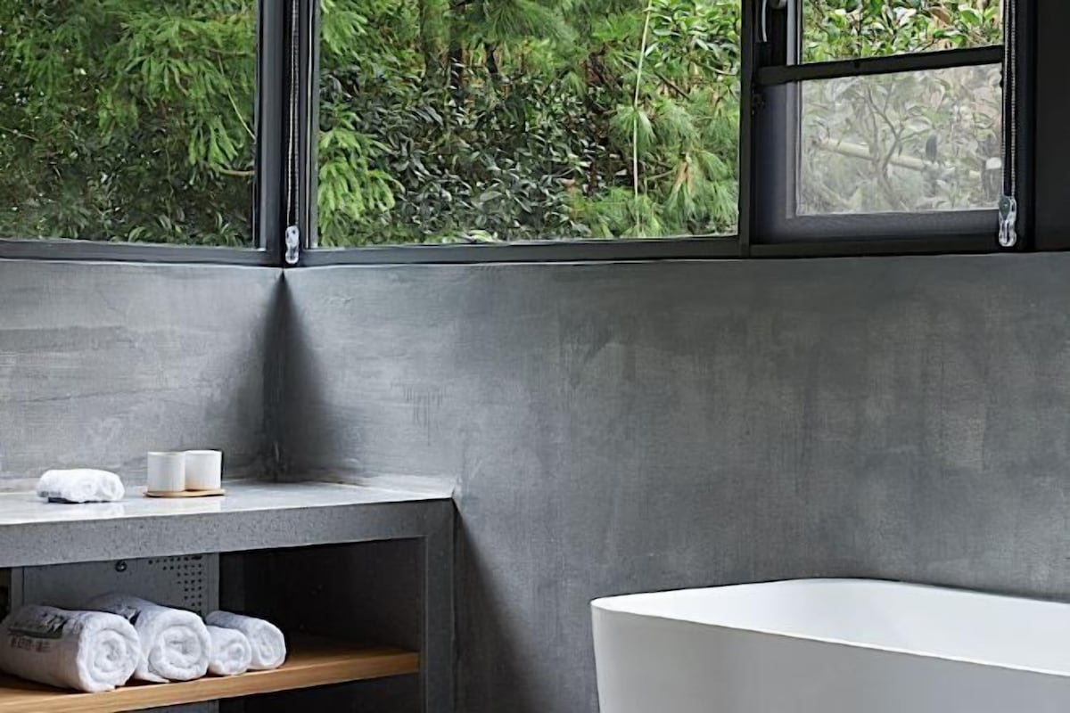 A modern bathroom with a bathtub, a shelf with towels, and a window with a view of greenery.
