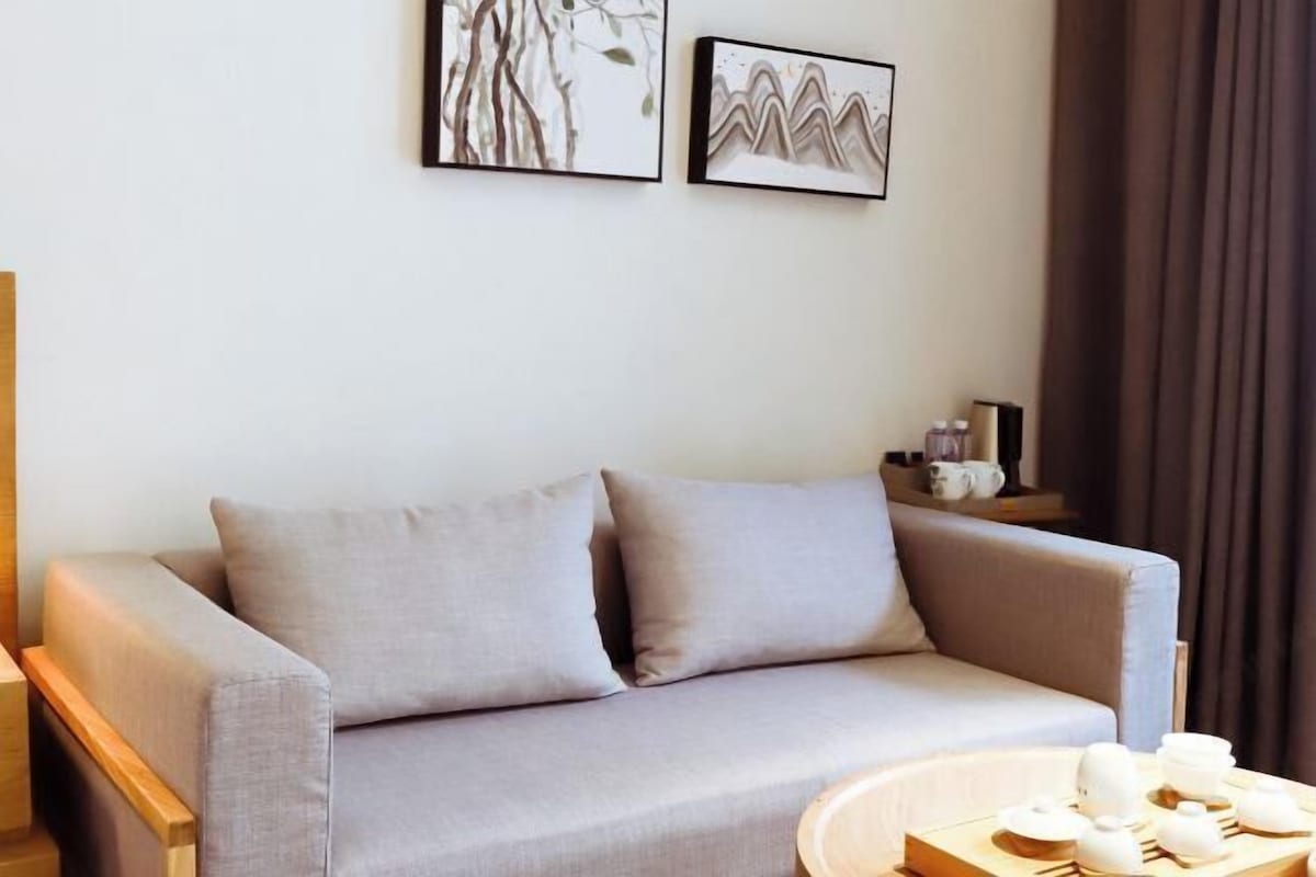 A modern living room with a grey sofa, two framed artworks on the wall, and a small table with teapots.