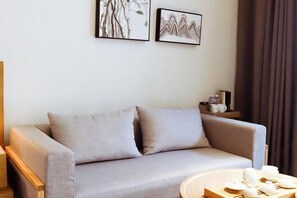 A modern living room with a grey sofa, two framed artworks on the wall, and a small table with teapots.