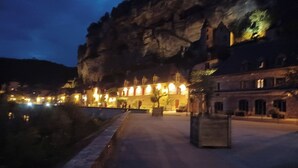 Un bâtiment historique doté d’une façade en pierre, d’une cour pavée et d’une rivière en premier plan.