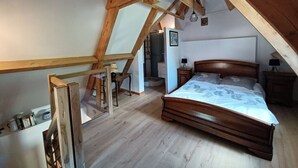 Une chambre avec un plafond en pente, des poutres en bois, un lit recouvert d’une couvre-lit à motifs, une table de chevet et une commode.