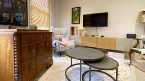 A modern living room with a wooden dresser, a round coffee table, a white sofa, and a flat-screen TV mounted on the wall. - Charming 2-bed Apt With 2 Bathtub Central London (London)