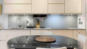A modern kitchen with white cabinets, a stainless steel sink, and a glass dining table with a woven placemat. - Charming 2-bed Apt With 2 Bathtub Central London (London)