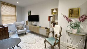 A modern living room with a flat-screen TV, a sofa, a coffee table, a chair, a small side table, and a bookshelf. - Charming 2-bed Apt With 2 Bathtub Central London (London)