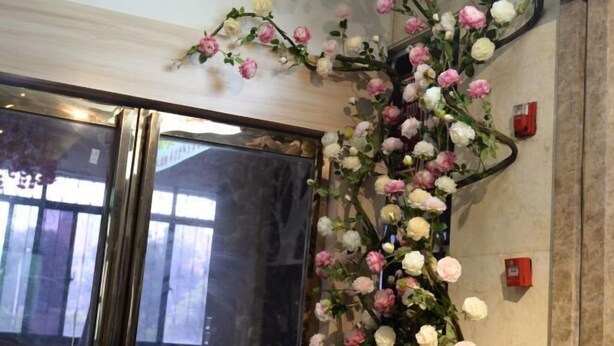 A hotel entrance with a large glass door, a wall-mounted artificial flower arrangement, and a fire alarm. - Yuedu Holiday Hotel (Yichun)