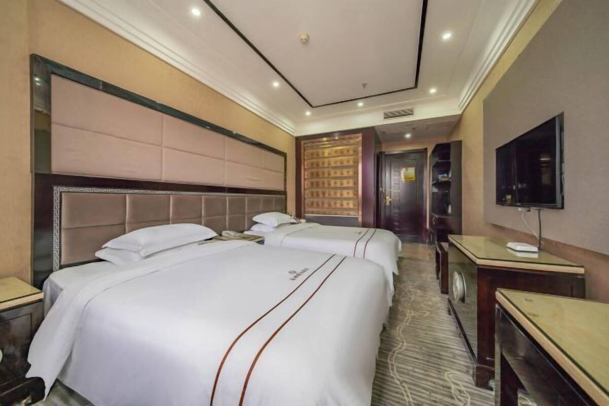 A hotel room with two beds, a television, and a desk.