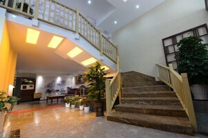 Un vestíbulo amplio con piso de mármol, una escalera con barandilla de madera y una planta grande en maceta.