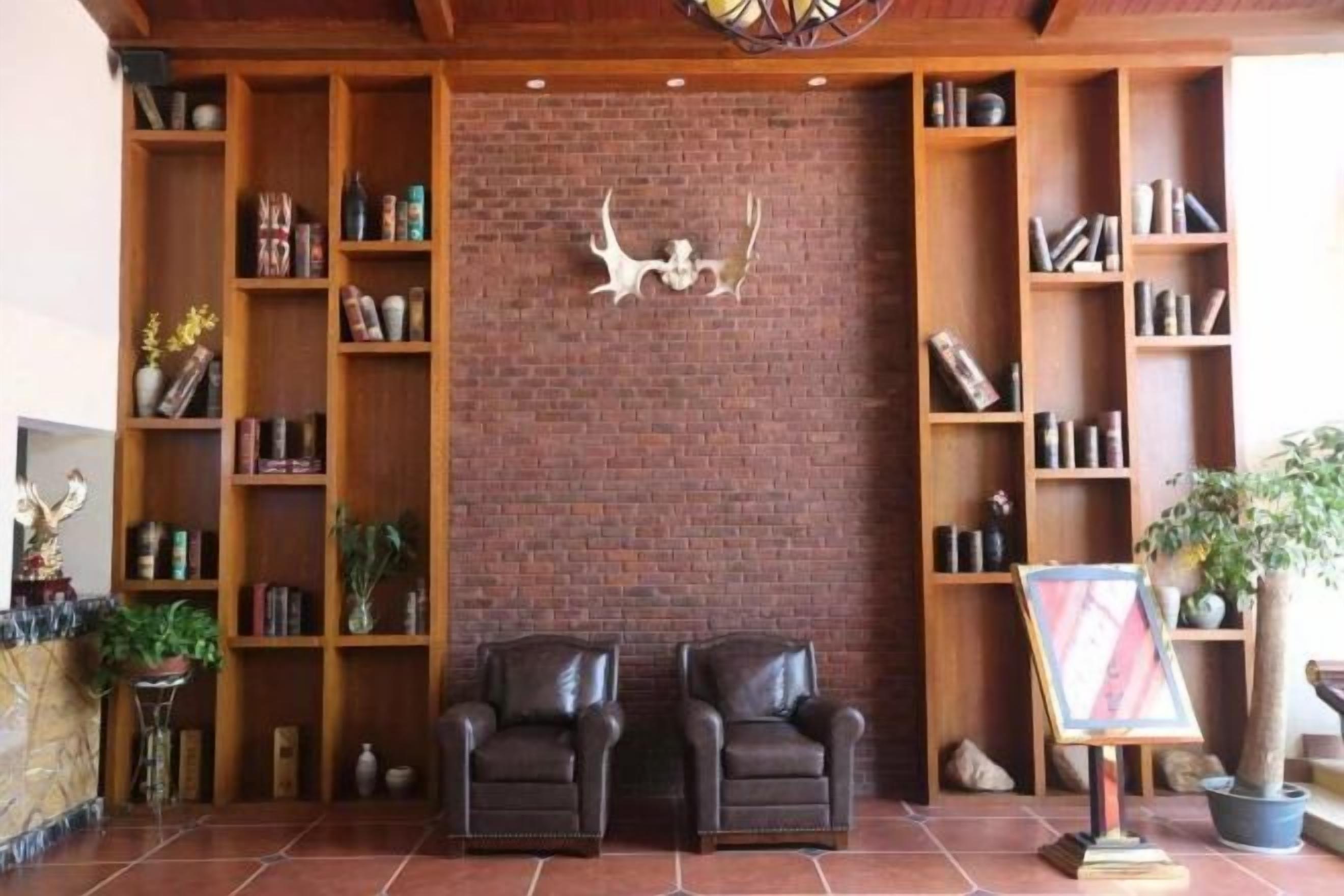 Een kamer met een bakstenen muur, houten boekenkasten, twee leren fauteuils en een kamerplant.