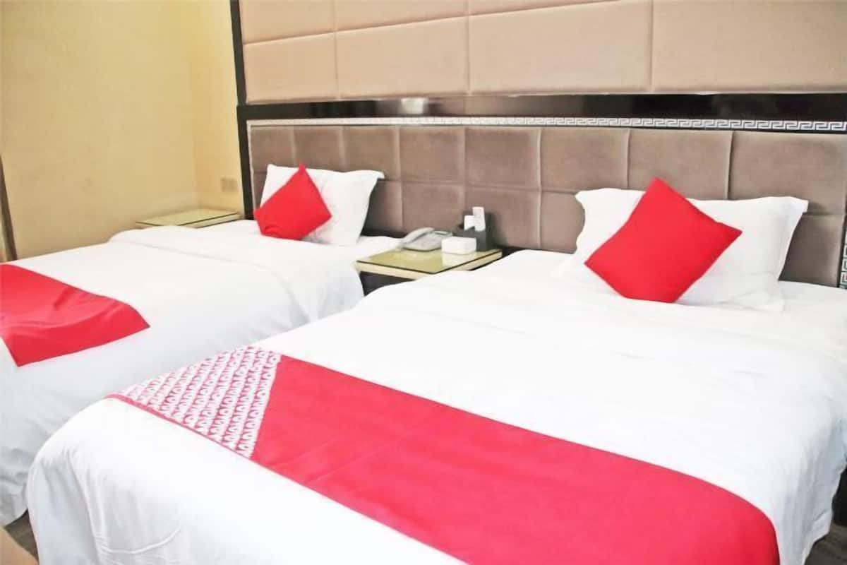 A hotel room with two beds, each with white bedding and red accents. There is a nightstand with a phone and a tissue box between the beds.
