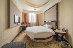 Una habitación de hotel con una cama grande, un escritorio con silla, un televisor y una mesita de noche con lámpara.