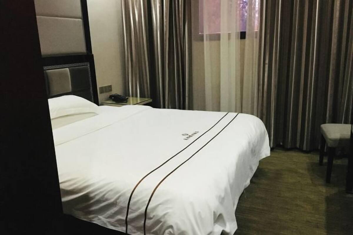 A hotel room with a bed, a nightstand, a chair, and a window with curtains.