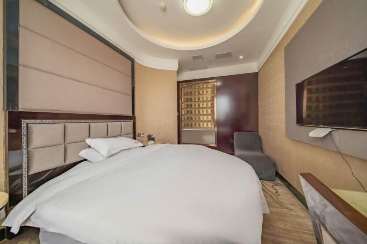 A hotel room with a large bed, a television, a seating area, and a door with a patterned design.