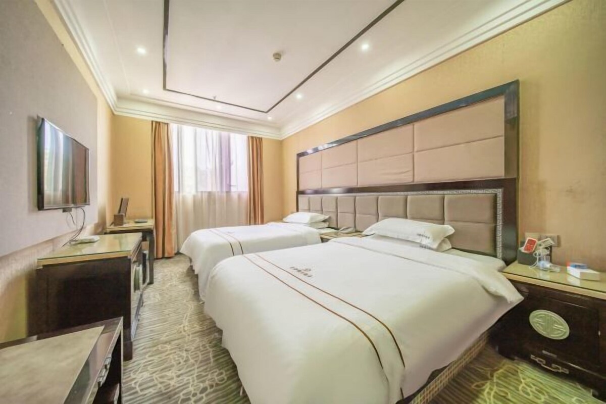 A hotel room with two beds, a desk, a chair, a TV, and a window with curtains.