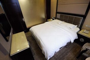Hotellihuone, jossa on sänky, yöpöytä ja pieni pöytä.