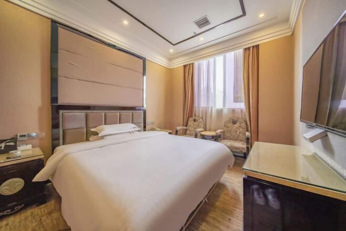 A hotel room with a large bed, a desk with a flat-screen TV, a chair, and a window with curtains.