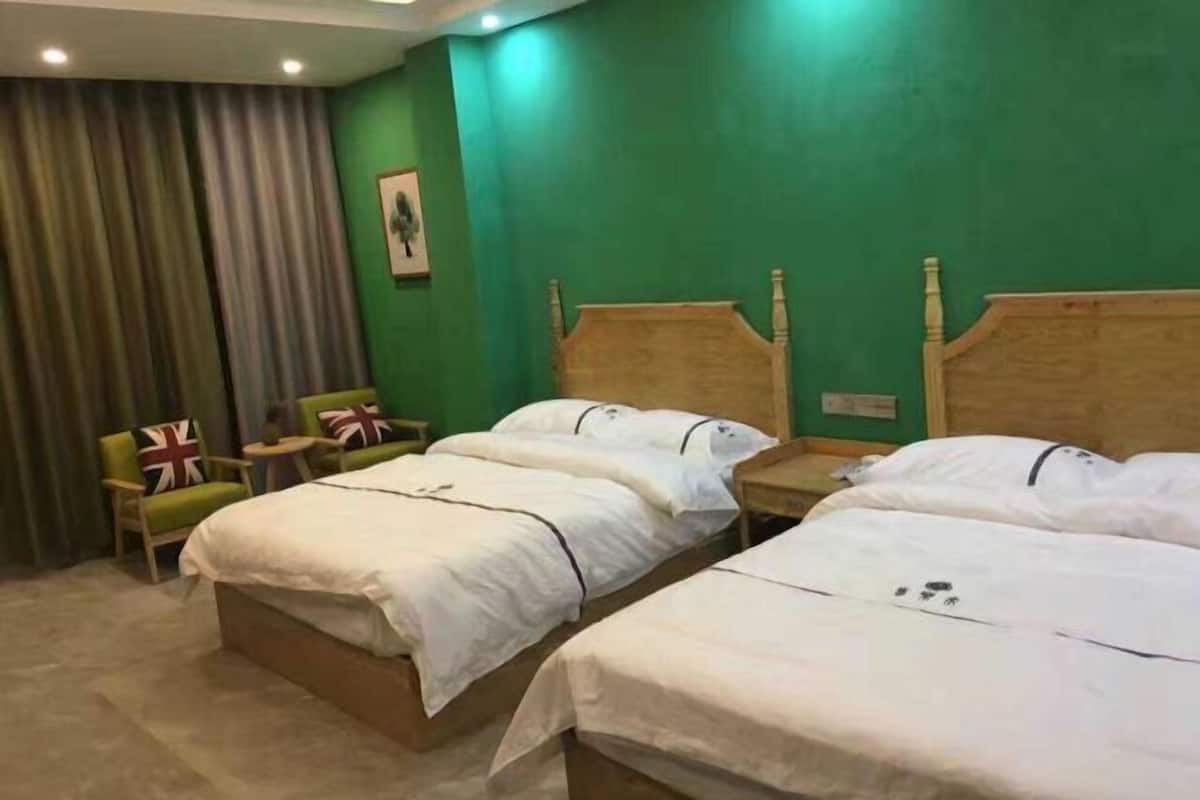 A hotel room with three beds, a green wall, and a curtain.
