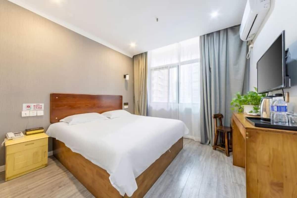 Ein Hotelzimmer mit einem hölzernen Bett, einem Nachttisch mit Telefon, einem Schreibtisch mit Computer und einem Fernseher.