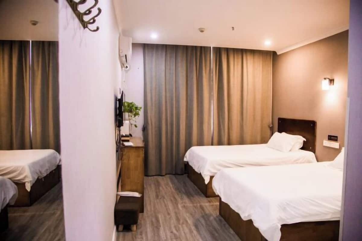 Ein Hotelzimmer mit zwei Einzelbetten, einem Holznachttisch, einem Schreibtisch mit Stuhl und einem großen Fenster mit Vorhängen.