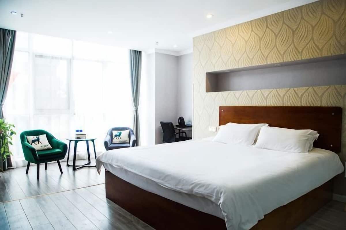 A hotel room with a large bed, a desk, a chair, and a small table.