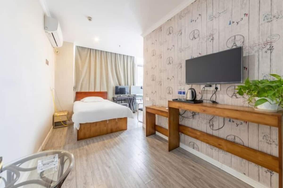 Ein Hotelzimmer mit einem Bett, einem Fernseher, einem Schreibtisch, einer Pflanze und einem fensterbepflanzten Fenster.