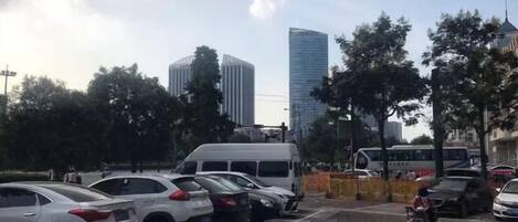 Un estacionamiento con autos y una motocicleta, rodeado de árboles y edificios.
