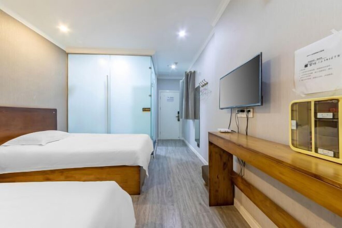 A hotel room with two beds, a wooden desk, a flat-screen TV, and a mirror.