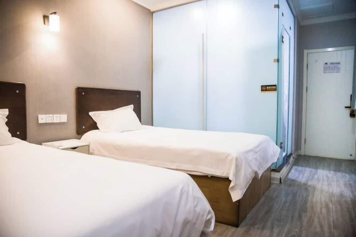 Ein Hotelzimmer mit zwei Einzelbetten, einem Nachttisch, einer Wandleuchte und einer Tür mit einem Schild.