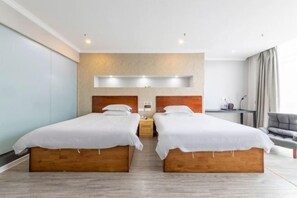 Une chambre d’hôtel avec deux lits simples, un bureau, une chaise et une grande fenêtre avec des rideaux.