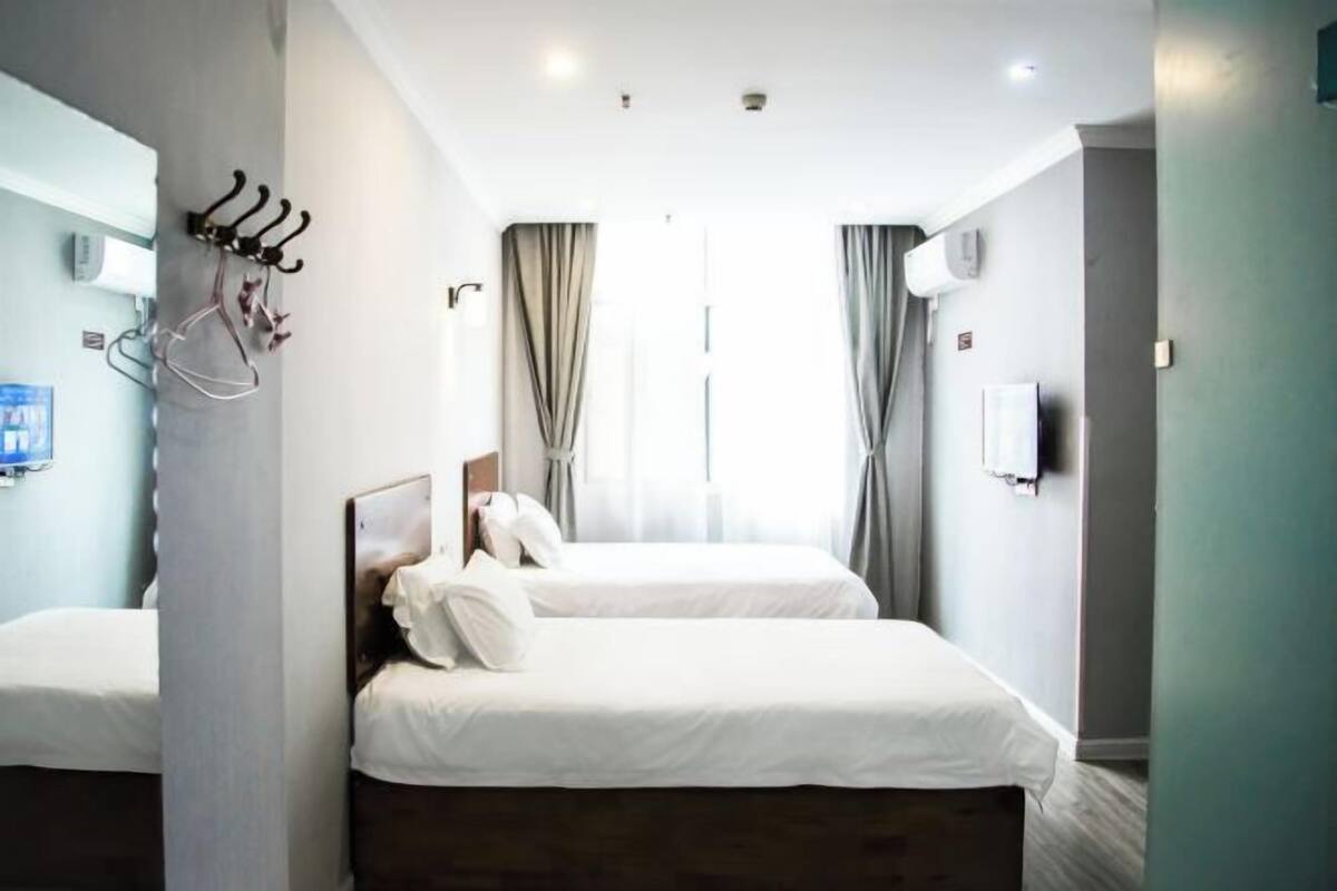 Ein Hotelzimmer mit zwei Betten, einem Spiegel, einem Kleiderständer und einem Fernseher.