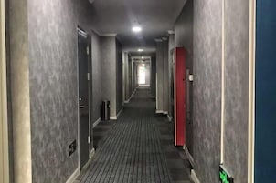 A corridor with doors on both sides, a trash bin, and a red object on the right.