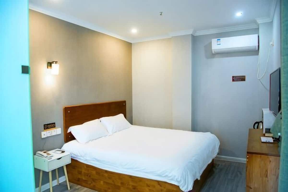 Ein Hotelzimmer mit Bett, Nachttisch, Lampe und einer Wand-Klimaanlage.