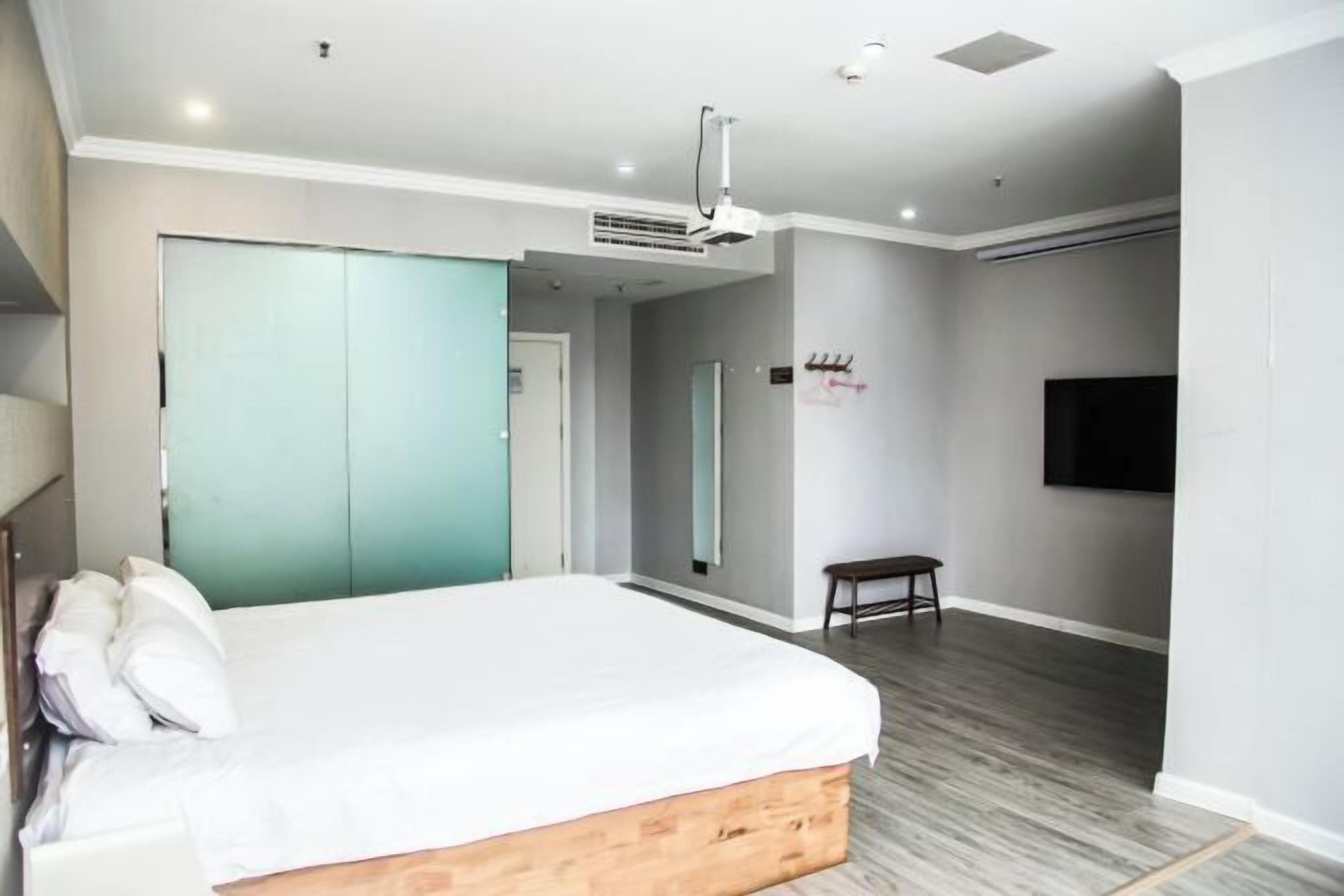 Quarto com cama, guarda-roupa, televisão e uma mesinha.
