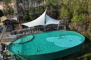 A large outdoor swimming pool with a white canopy, surrounded by trees and a small building with a staircase. - Cotton Tiankeng Hotel (Luocheng)