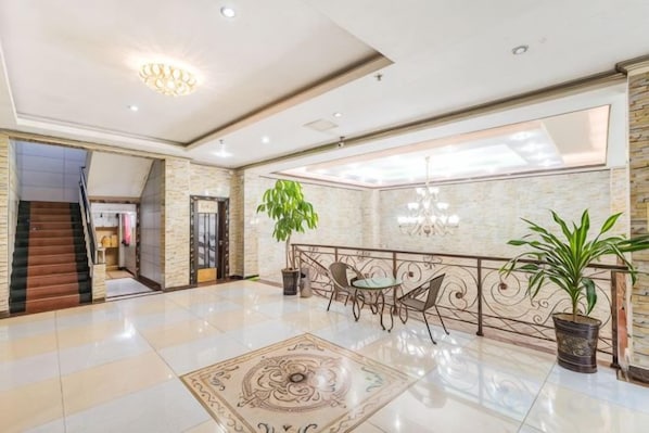 A spacious lobby with a marble floor, a staircase, a dining area with chairs and a table, and a large potted plant.