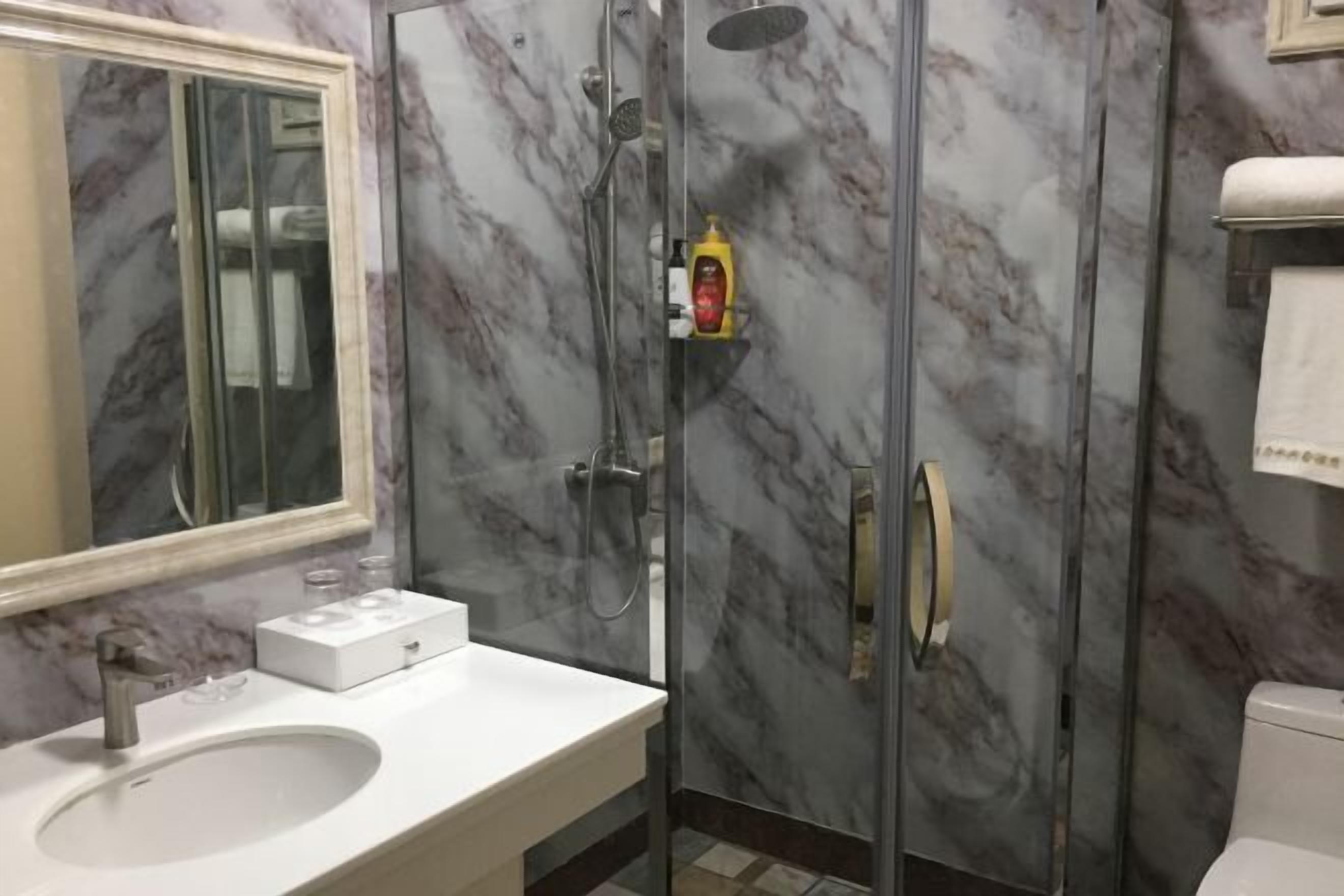 Kylpyhuone, jossa on marmoriseinä, lasiseinäinen suihku, valkoinen pesuallas ja wc.