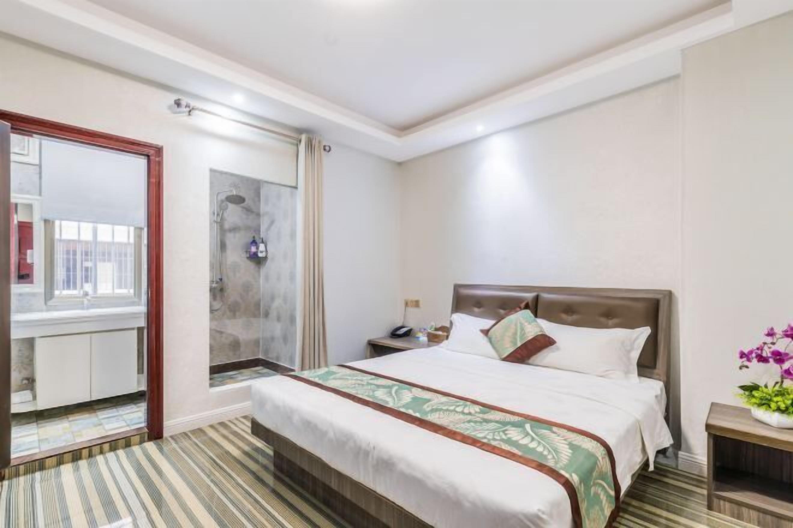 A hotel room with a large bed, a bedside table, a mirror, and a view of the outside.